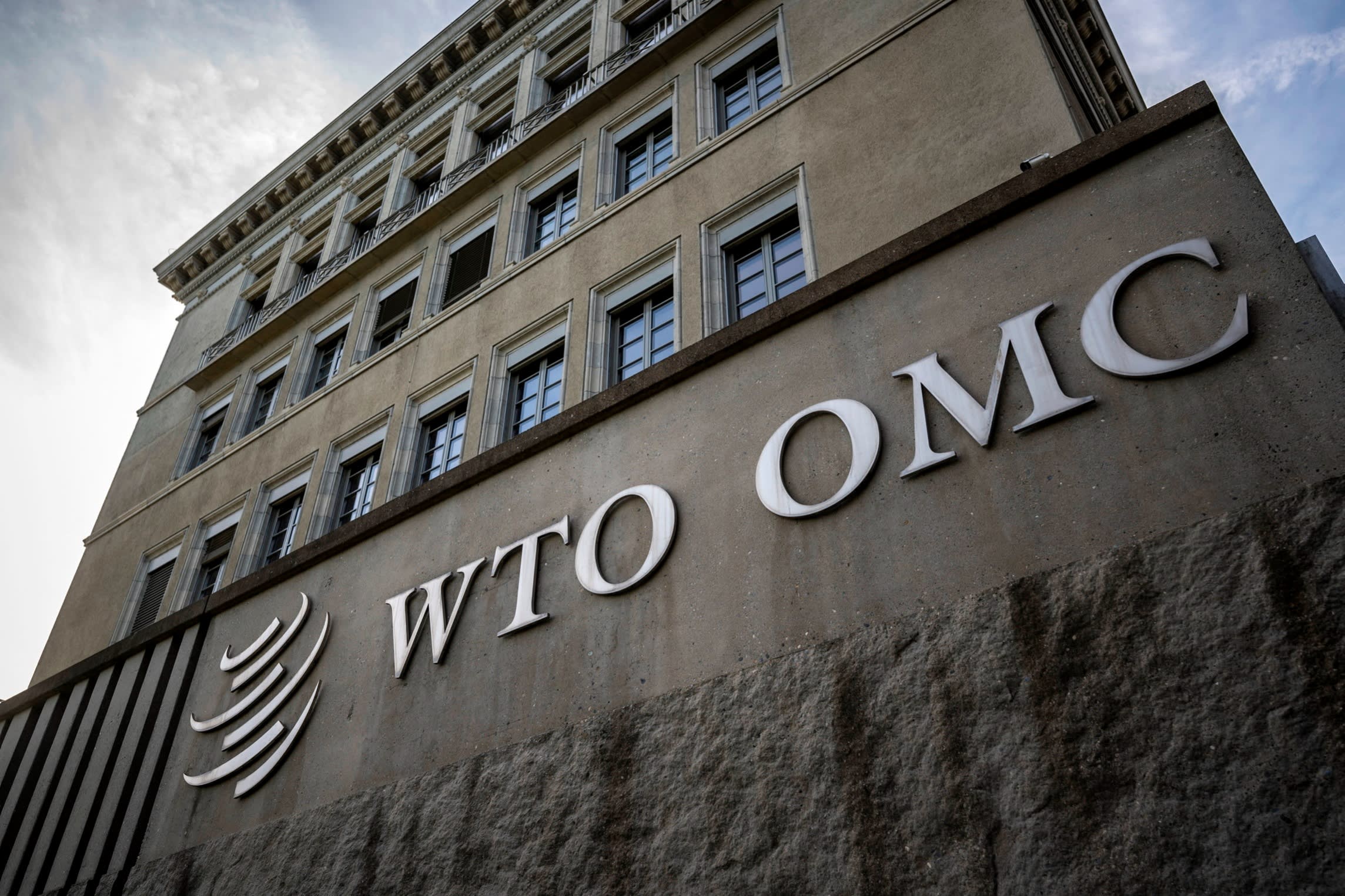 The exterior of a building with a large WTO OMC logo on a stone wall