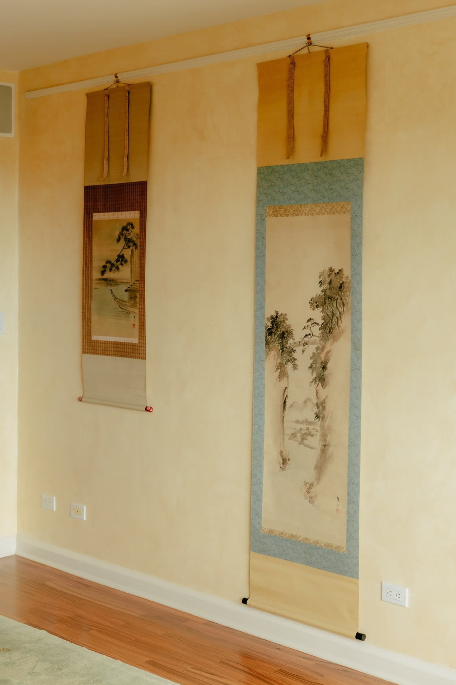 Two Japanese hanging scrolls, featuring ink and colour paintings, hang on the pale interior wall of an American home