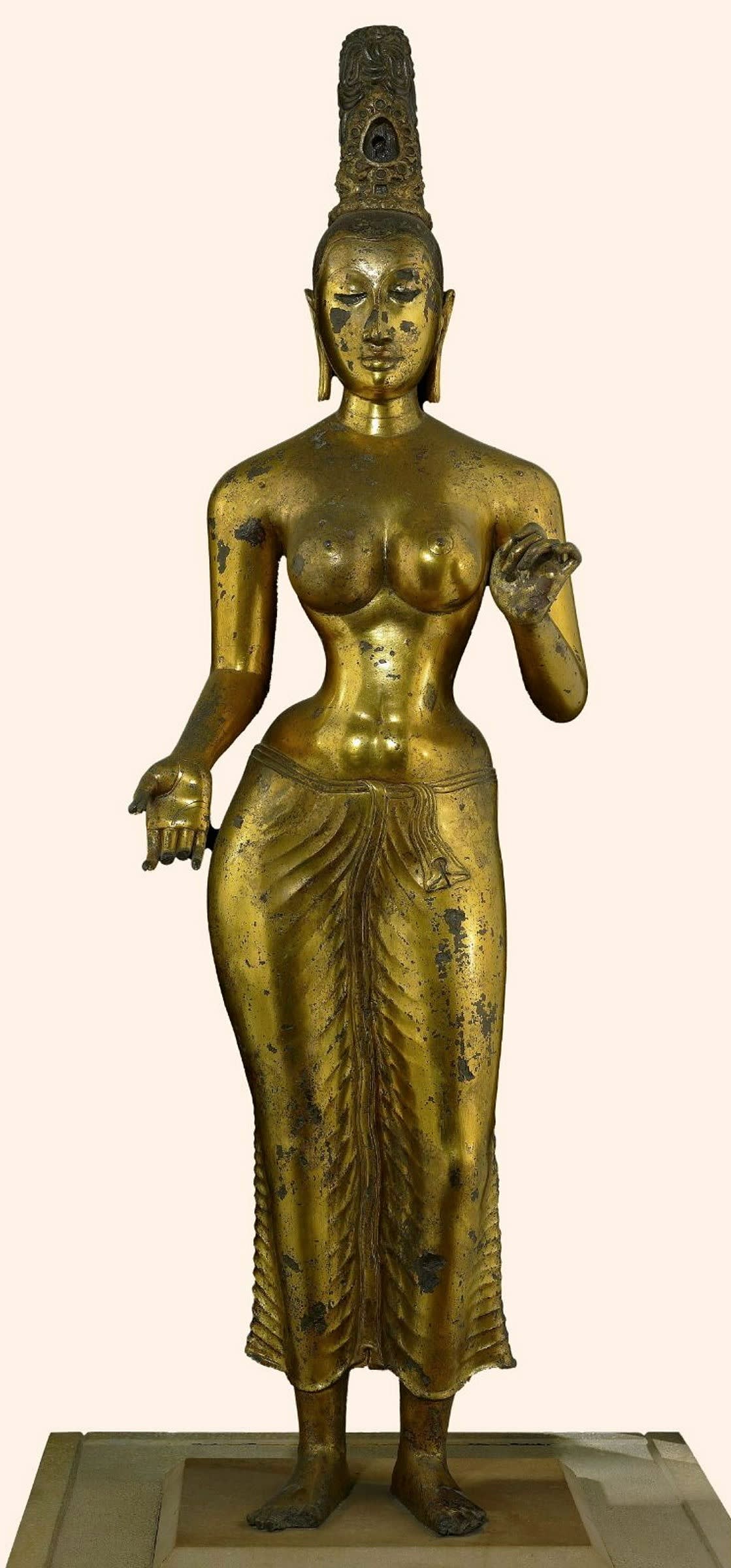 A gold figurine of a woman with tall hair and a long dress with her arms extended