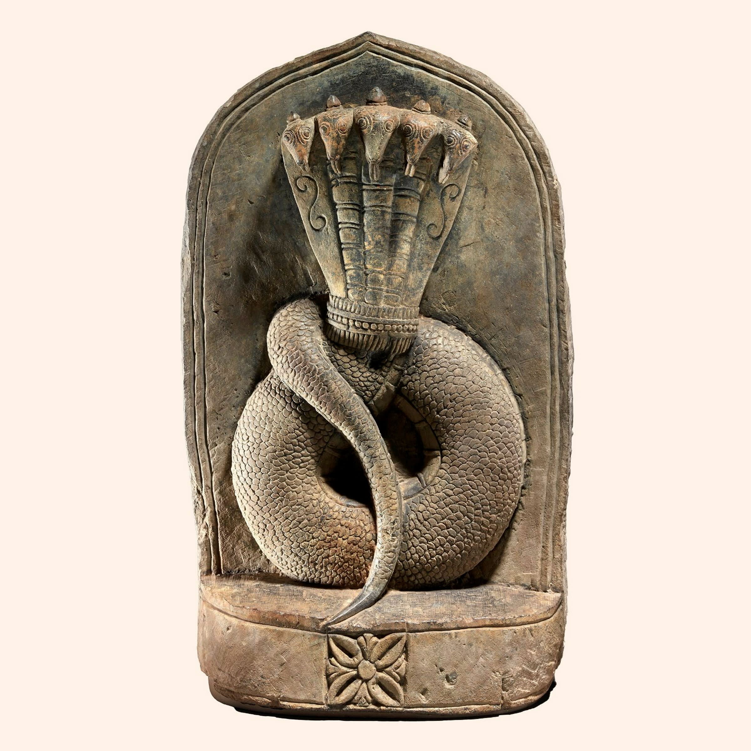 A stone sculpture of a snake-like creature in the shape of a circle with a tail draped over it and a fan-like object on the top 