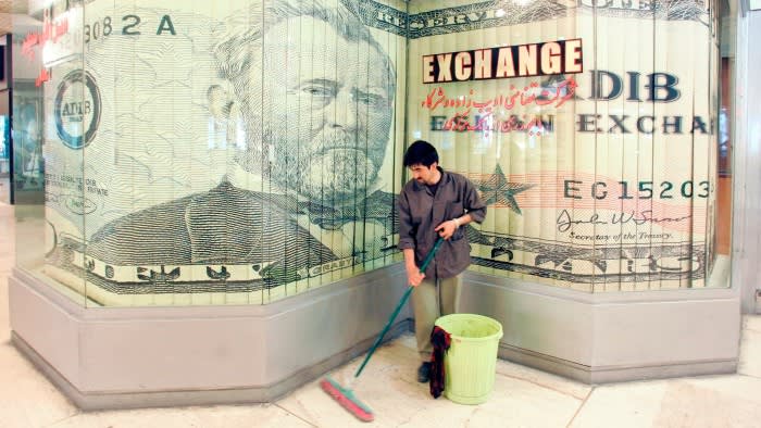 A male cleaner sweeps the floor in front of a currency exchange shop which has a large $50 bill in the window
