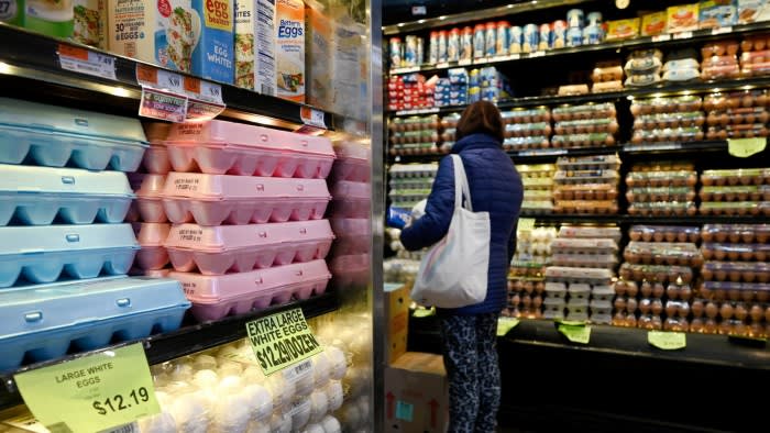 A woman stands in front of eggs placed on refrigerated shelves in a New York supermarket