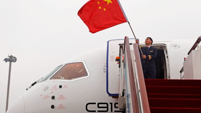 A man waves a Chinese flag while standing at the entrance of a C919 aircraft