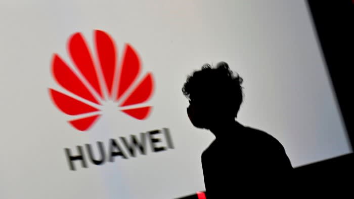 A person walks past a large screen displaying the Huawei logo