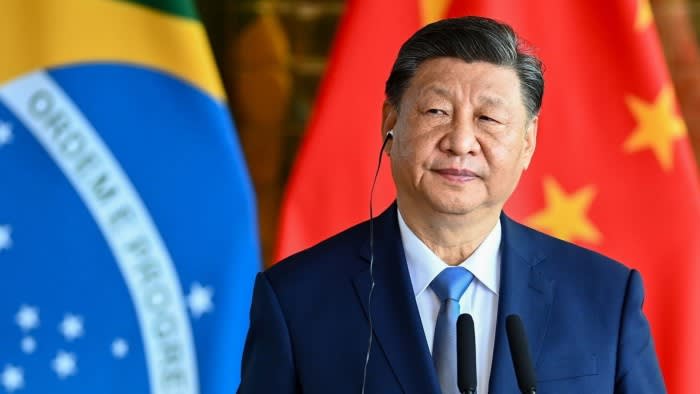 Xi Jinping stands at a podium with an earpiece in front of Brazilian and Chinese flags during a news conference