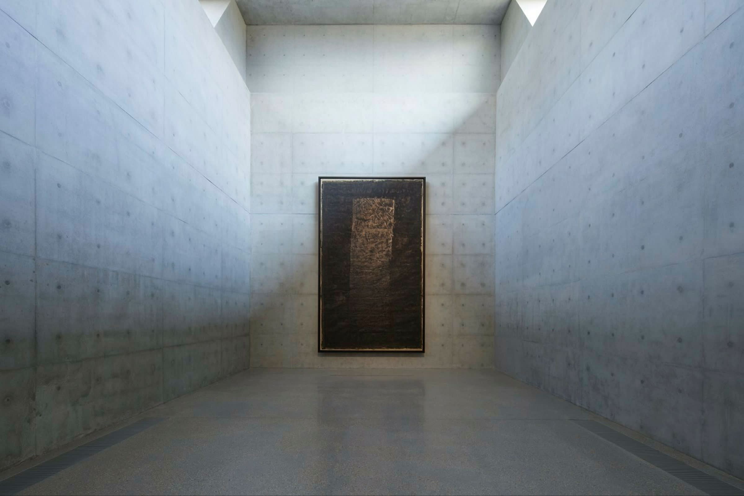 Dark rectangular work, painted using black ink and alum on paper, placed vertically at the end of a long, narrow room with white walls made from the kind of large stonemasonry traditionally used in a castle or abbey