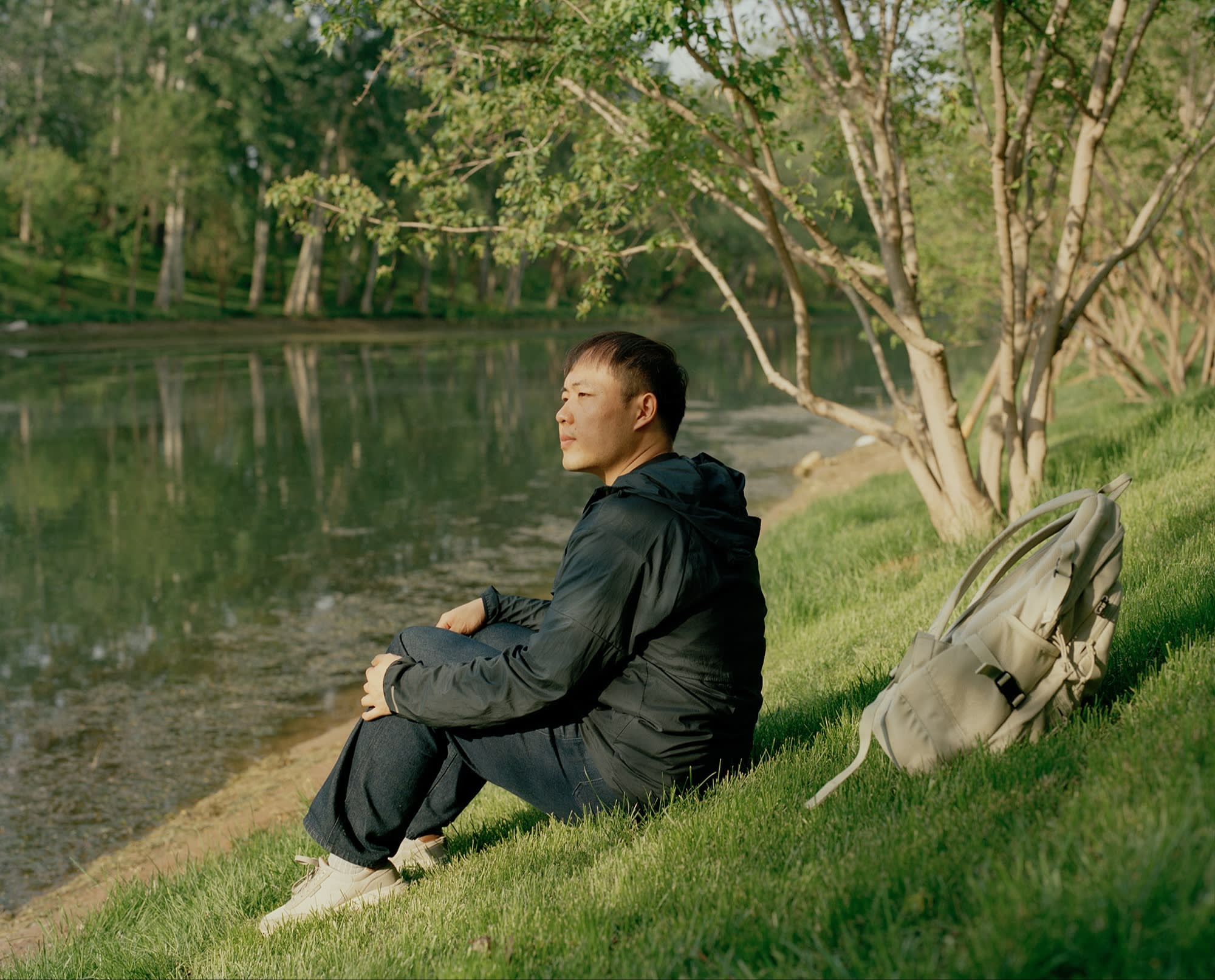 A man sits by a peaceful river in a park