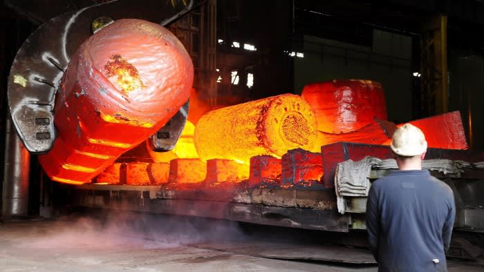 A worker in a hard hat stands in front of glowing red hot metal being moved across a heavy forge at the Forgemasters works in Sheffield