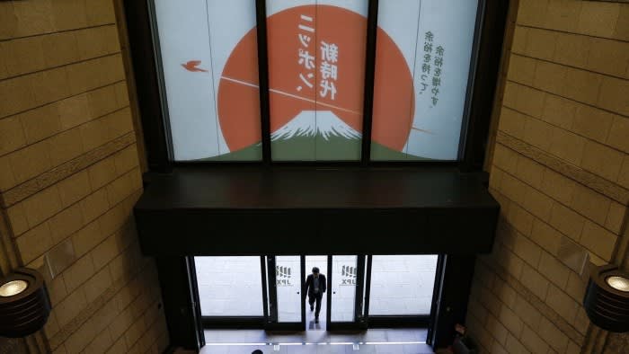 A person enters the Tokyo Stock Exchange building. The entrance is adorned with a large graphic featuring Mount Fuji and Japanese text against a backdrop of a red sun.