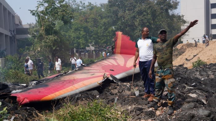 People stand near debris at the site of a plane crash near Sardar Vallabhbhai Patel International Airport