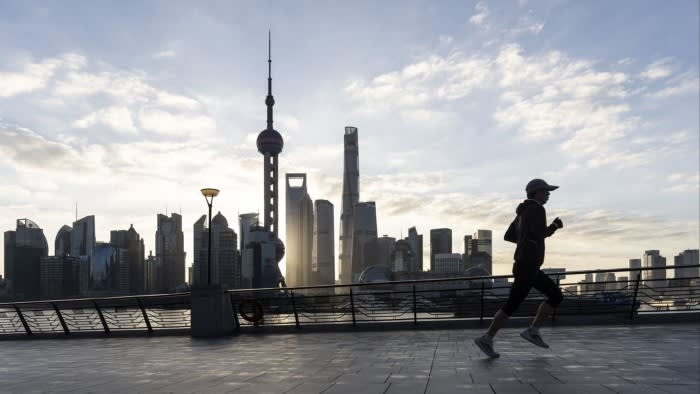 A person jogs along the Bund, silhouetted against the skyline of Pudong's Lujiazui Financial District in Shanghai. The Oriental Pearl Tower and other skyscrapers are visible in the background under a partly cloudy sky.