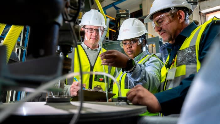 People in hard hats look at a machine