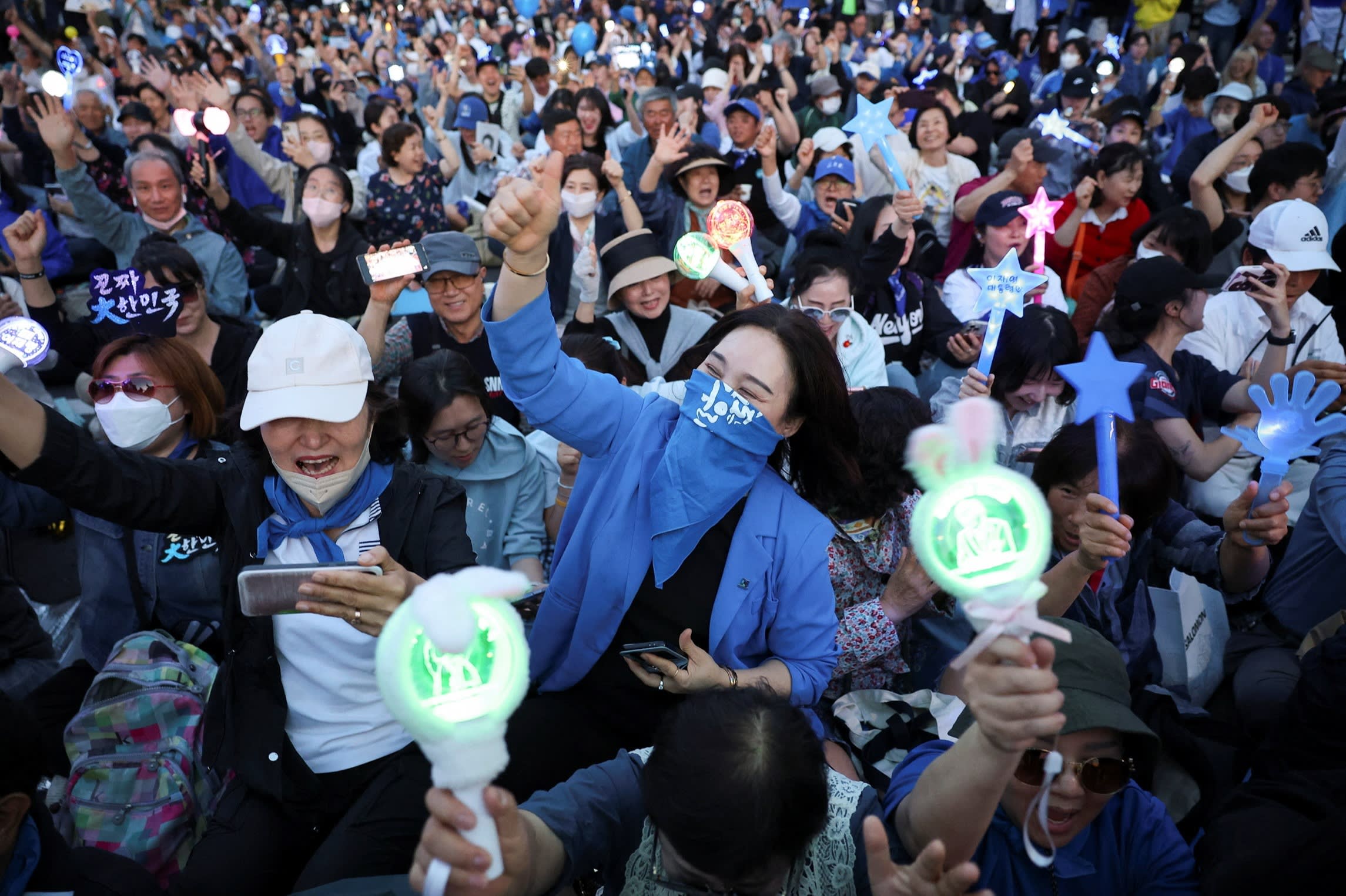 Supporters of Lee Jae-myung enthusiastically react to an exit poll report on the presidential election. They are holding illuminated signs and cheering