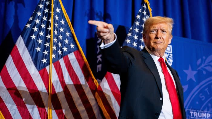 Donald Trump standing in front of two big US flags and pointing