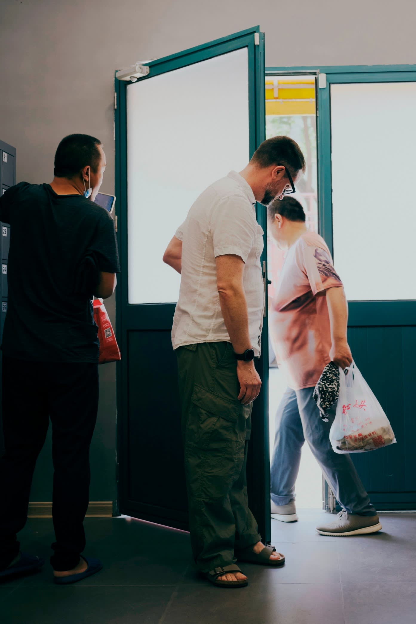 A man holds open the door for another man who walks out holding a carrier bag