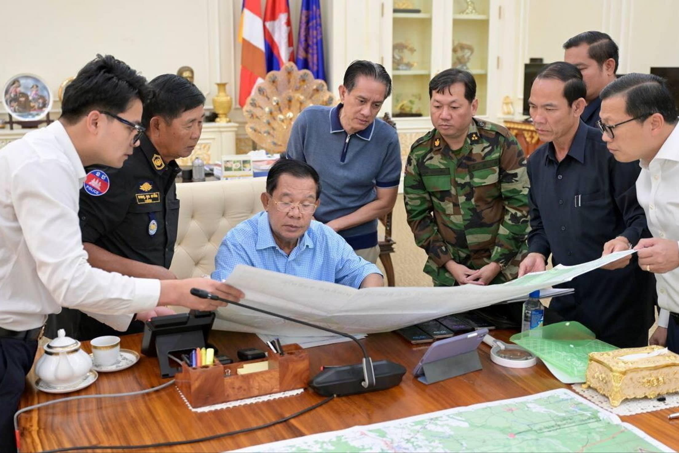 Hun Sen at a desk looking at a large map while surrounded by officials