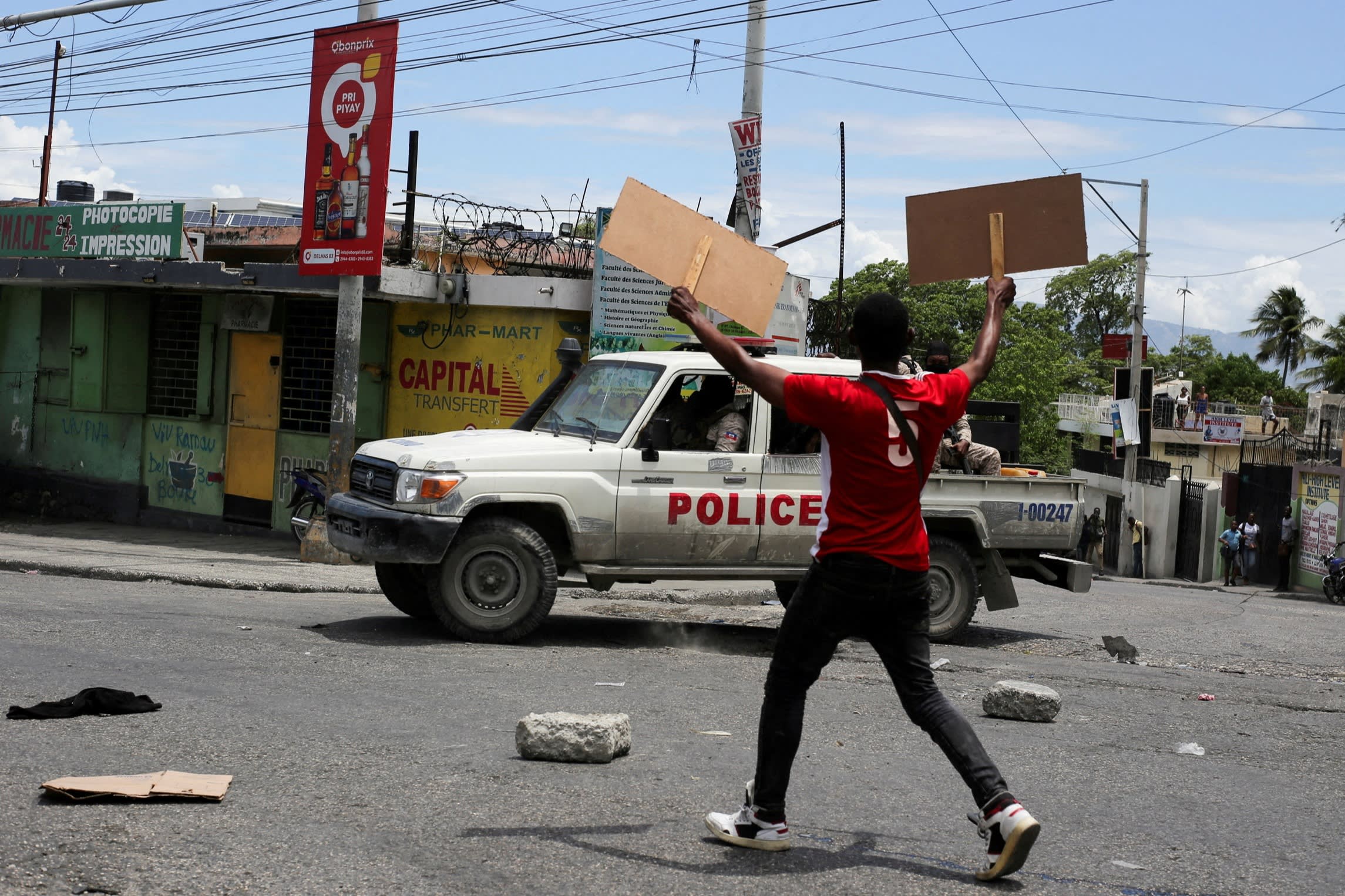 A man holds up placards as he yells towards a patrol car during a protest against gang-related violence