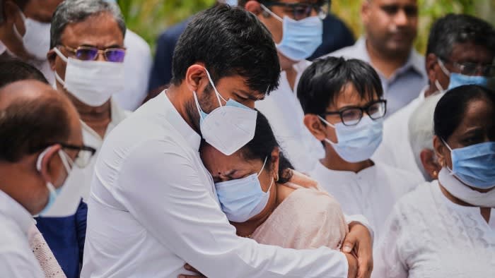Anjali Rupani, wearing a surgical mask is embraced by her son, also wearing a surgical mask, surrounded by other mourners