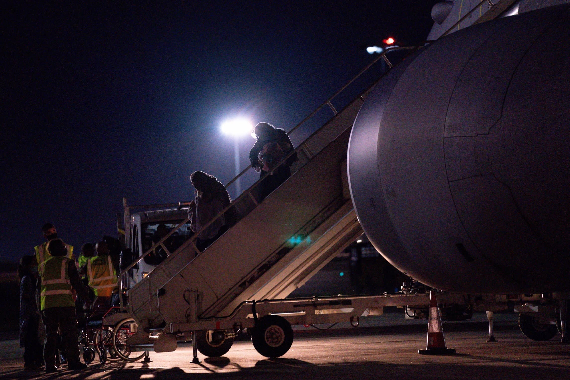 People descend the steps of an aircraft at night at RAF Brize Norton. Some are carrying children.