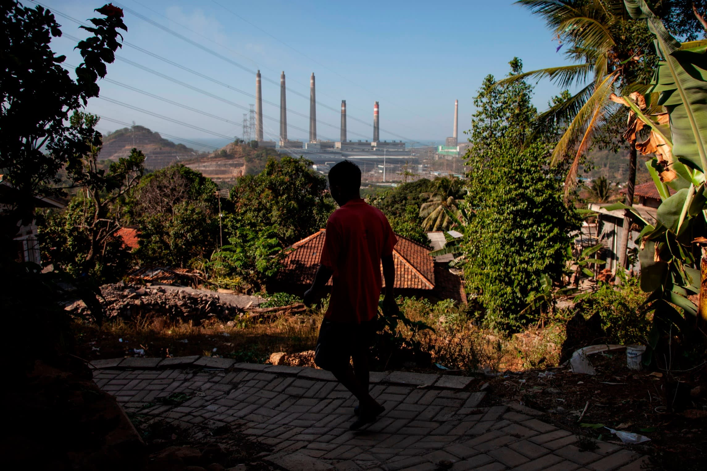 Villagers pass by on the village road as smoke ash spews from the chimney of the coal power plant owned by Indonesian Power in Cilegon, Banten province