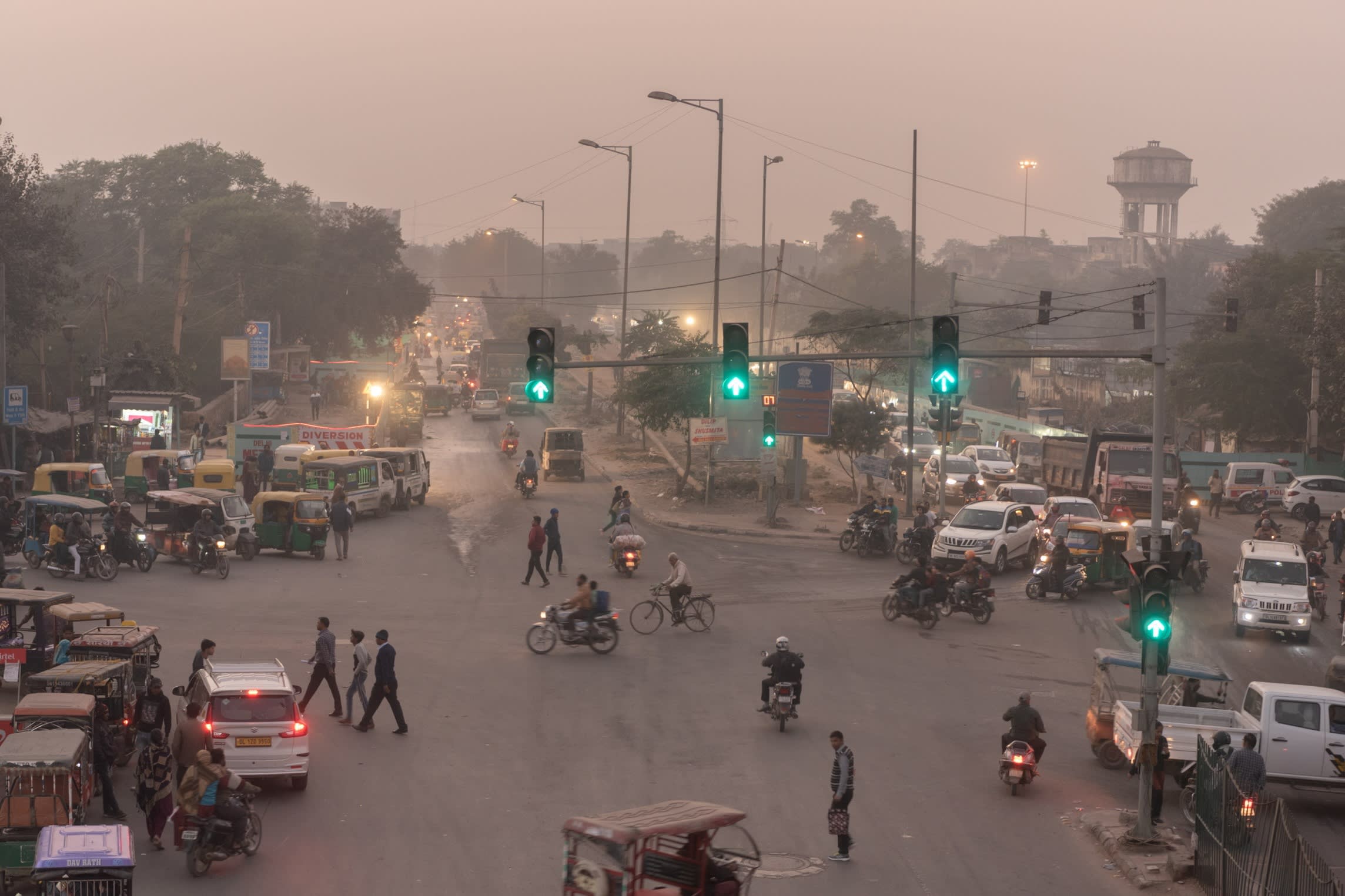 A crossroads, busy with cars, bikes and tuk-tuks, on a smoggy day