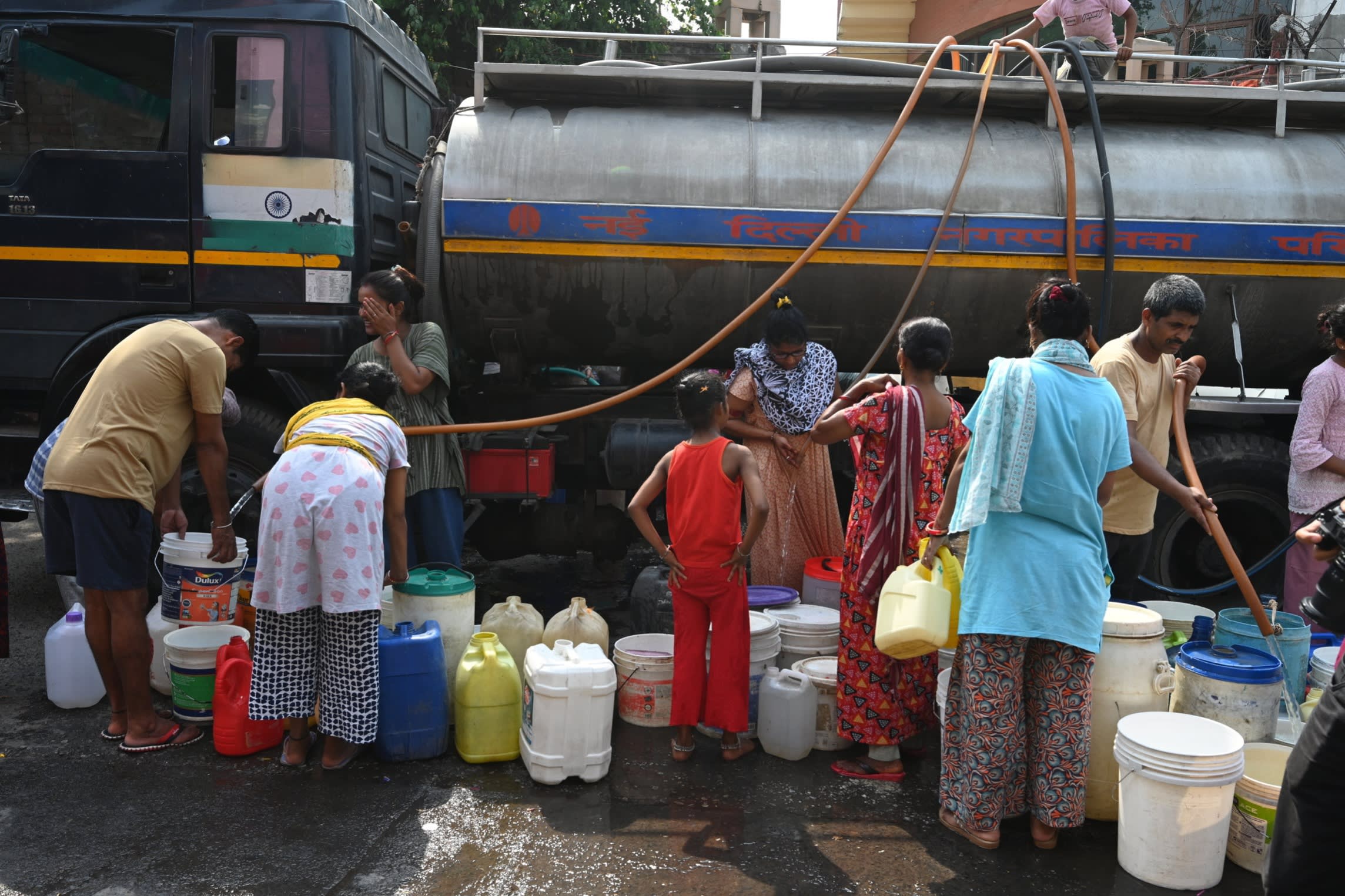 People pour water into plastic containers via hoses attached to a tanker 