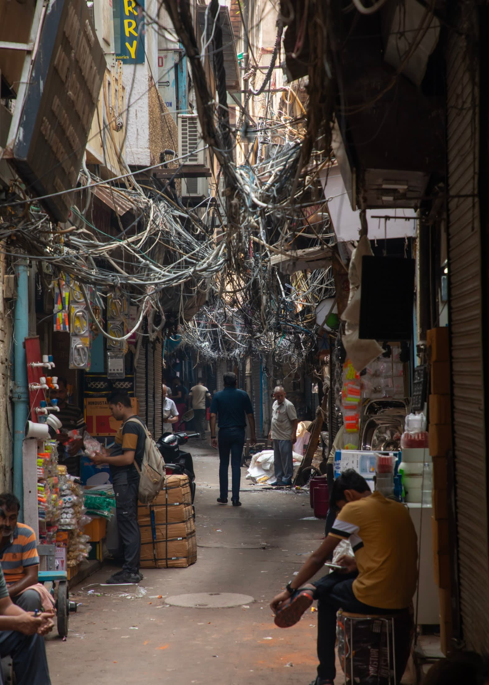A narrow alley lined by shops and houses with a tangle of power cables dangling above it