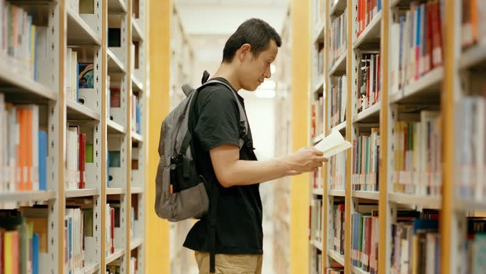 A man reads a book between bookshelves in a library