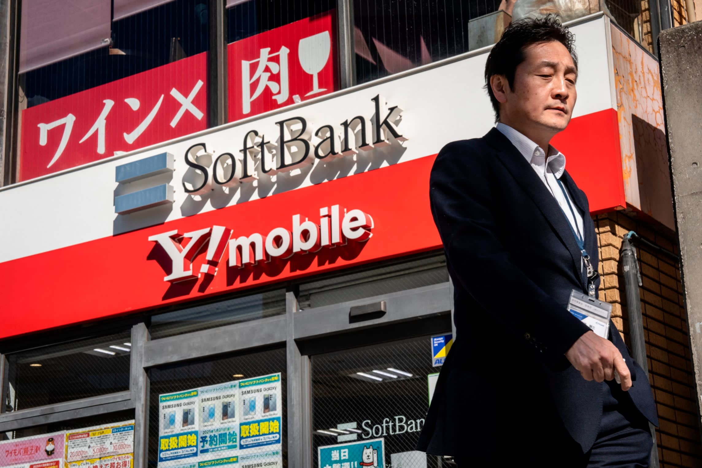 A man past signs for SoftBank and Y!mobile outside a telecommunications shop in Tokyo.