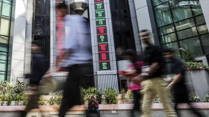 Employees walk past electronic boards displaying stock figures in the atrium of the National Stock Exchange of India building in Mumbai
