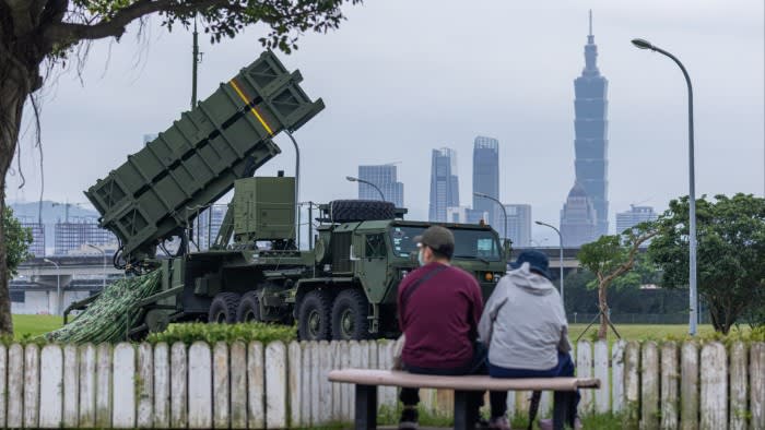 Two people sit on a park bench in Taipei, Taiwan in front of a Patriot air defence system on July 14 2025