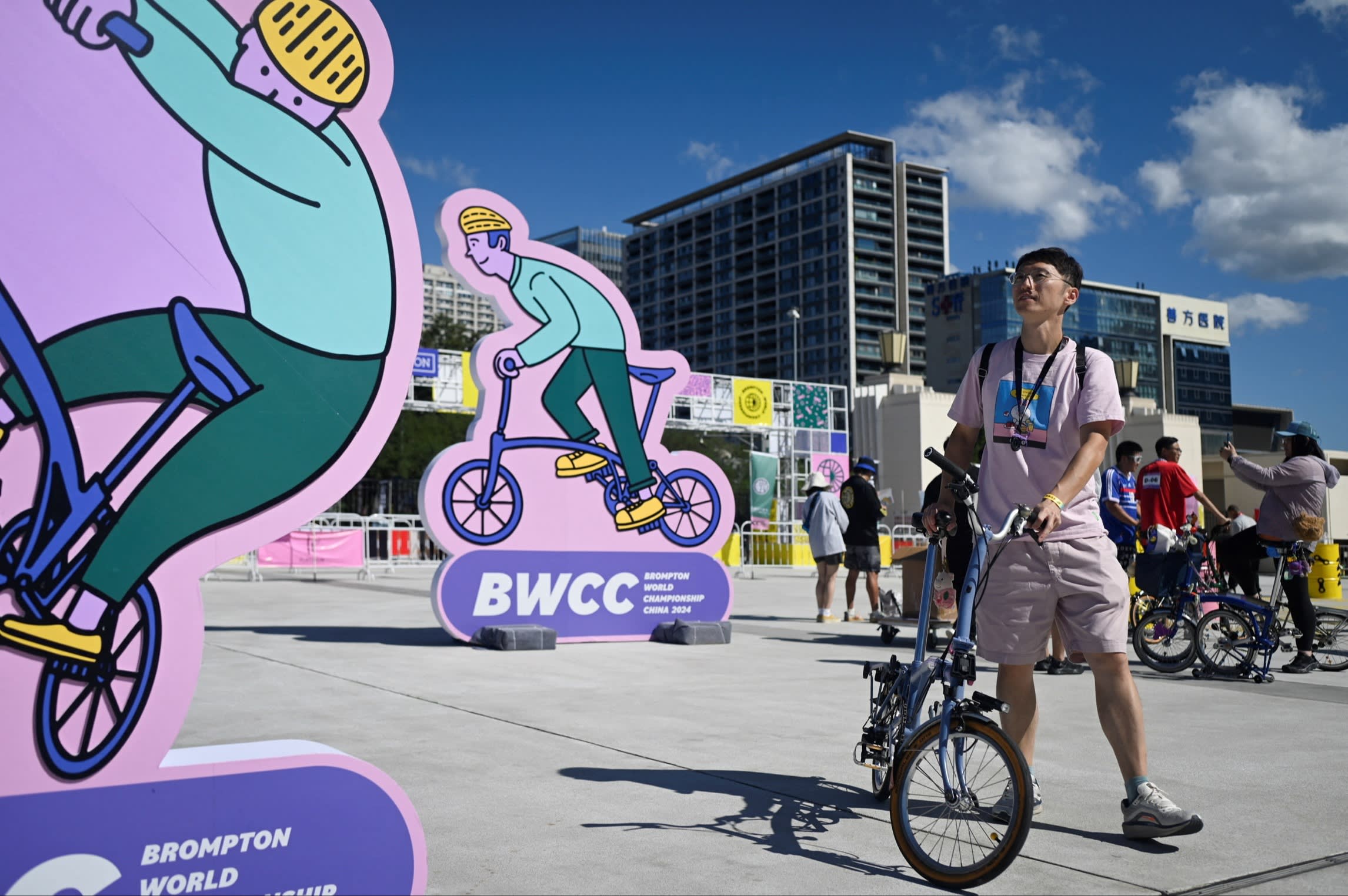 A rider with his bike in front of placards promoting the Brompton World Championship in September 2024