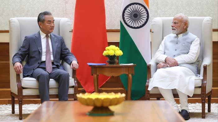 Narendra Modi and Wang Yi seated facing each other, with Chinese and Indian flags between them.