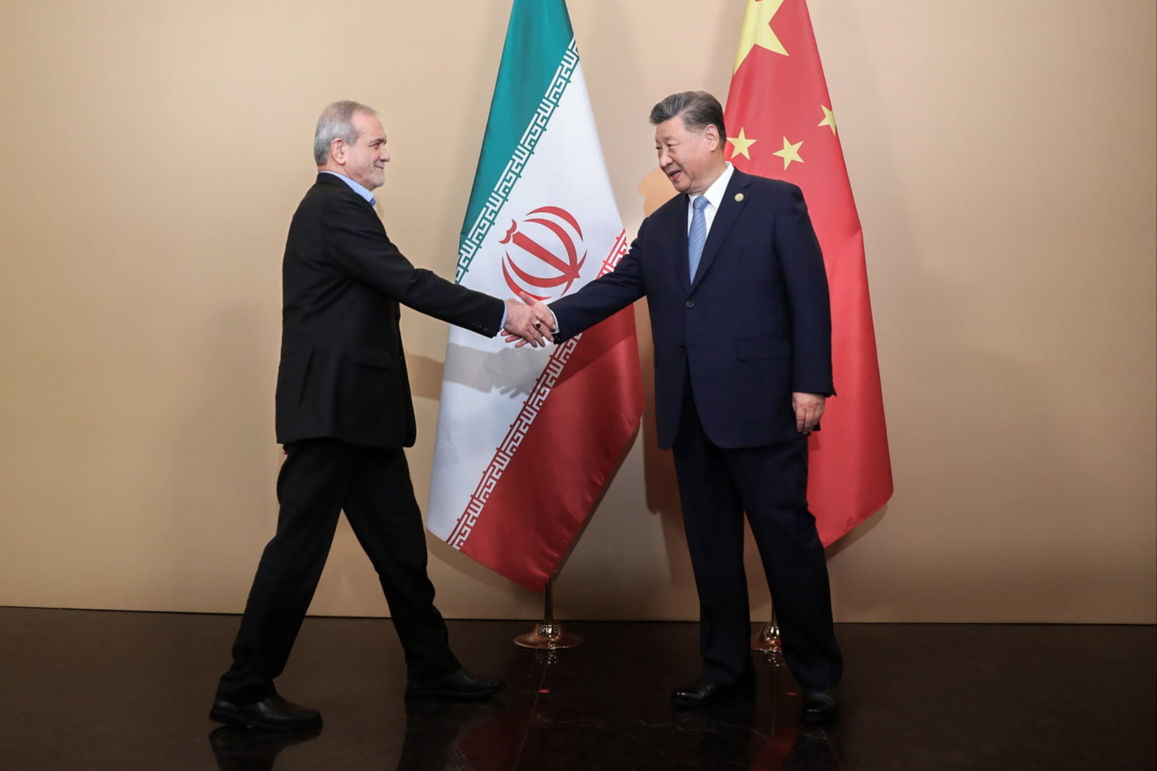 Xi Jinping and Masoud Pezeshkian shake hands in front of their national flags