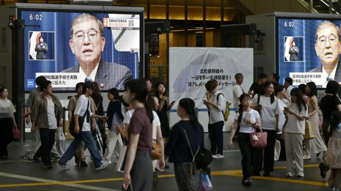 Street monitors display Japanese Prime Minister Shigeru Ishiba announcing his resignation as people walk by in Osaka