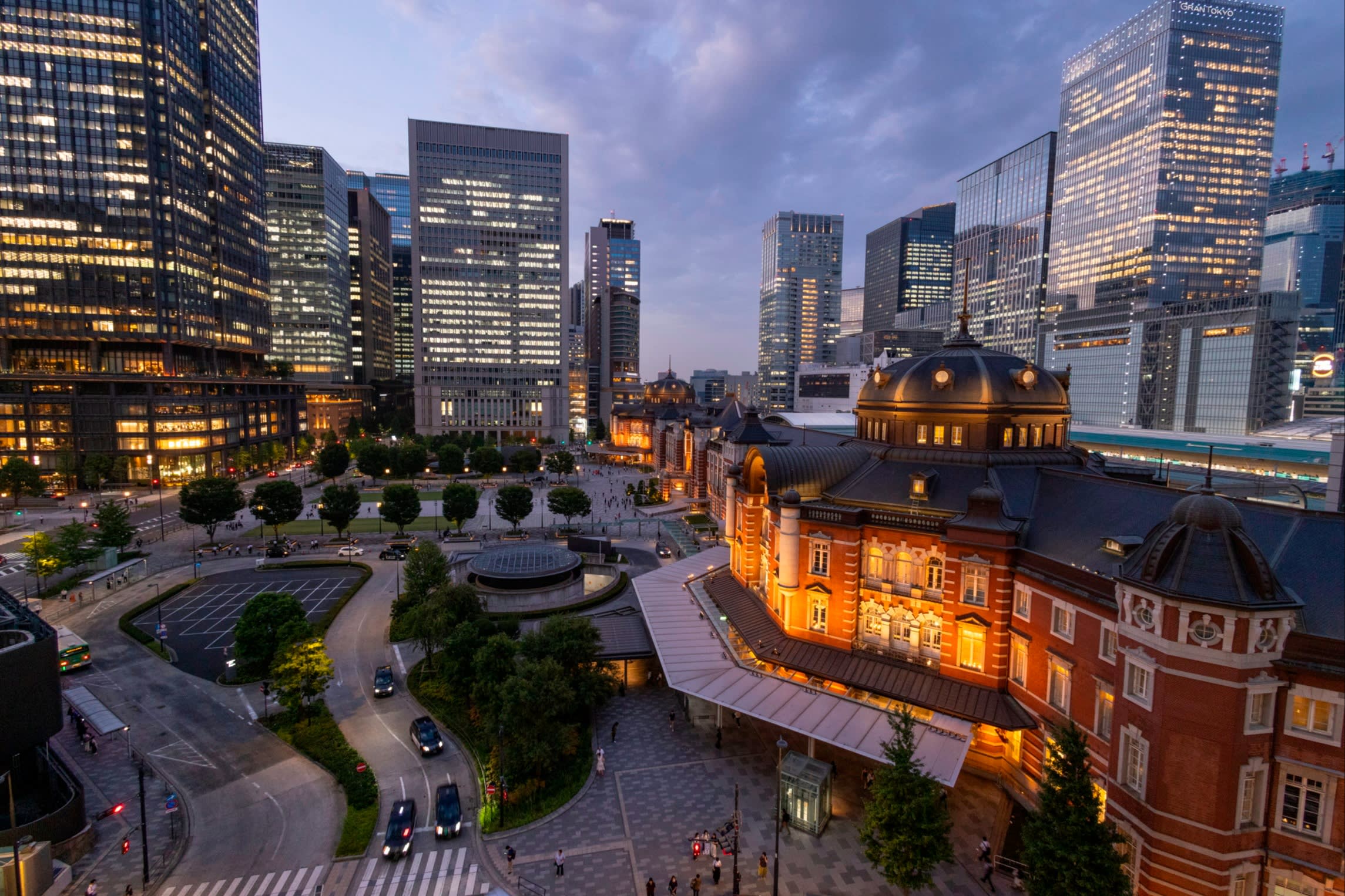 Tokyo Station’s red-brick building is illuminated at dusk, surrounded by modern skyscrapers in the Marunouchi financial district.