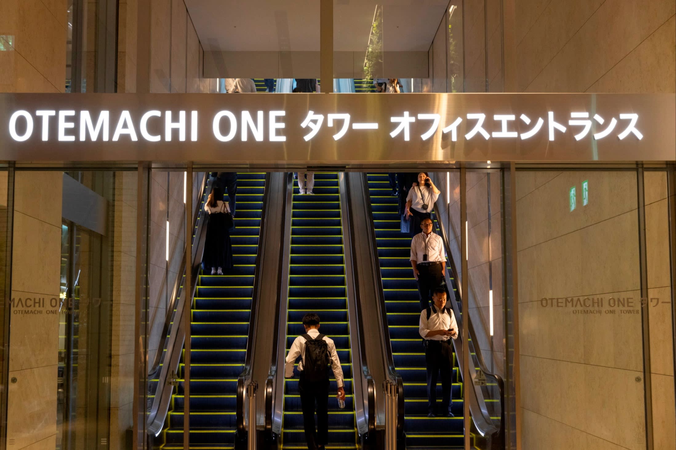 People ride escalators beneath a sign reading “OTEMACHI ONE” at the entrance of the Otemachi One building in Tokyo