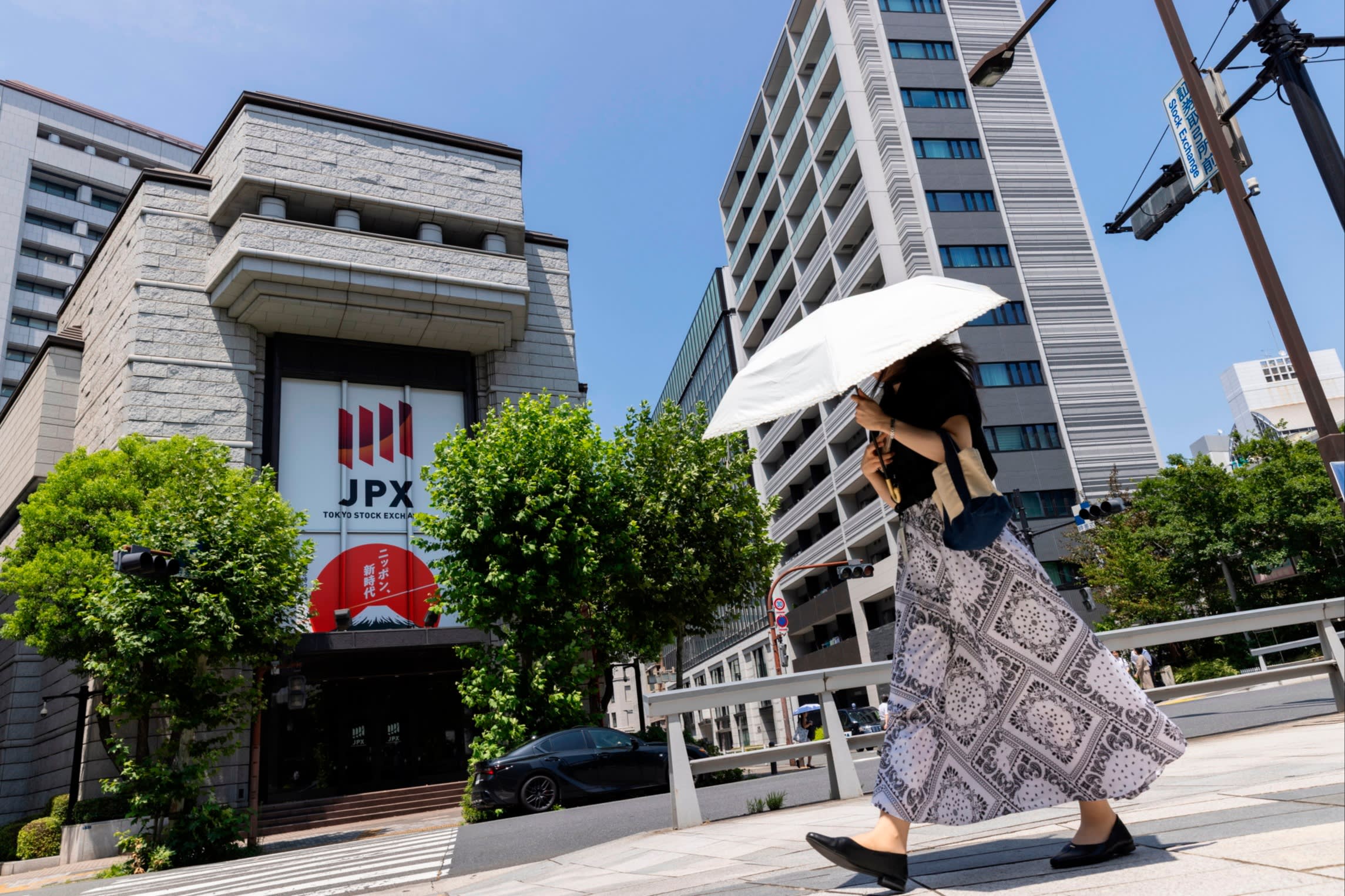 A woman holding a white umbrella walks past the Tokyo Stock Exchange building in Tokyo’s financial district