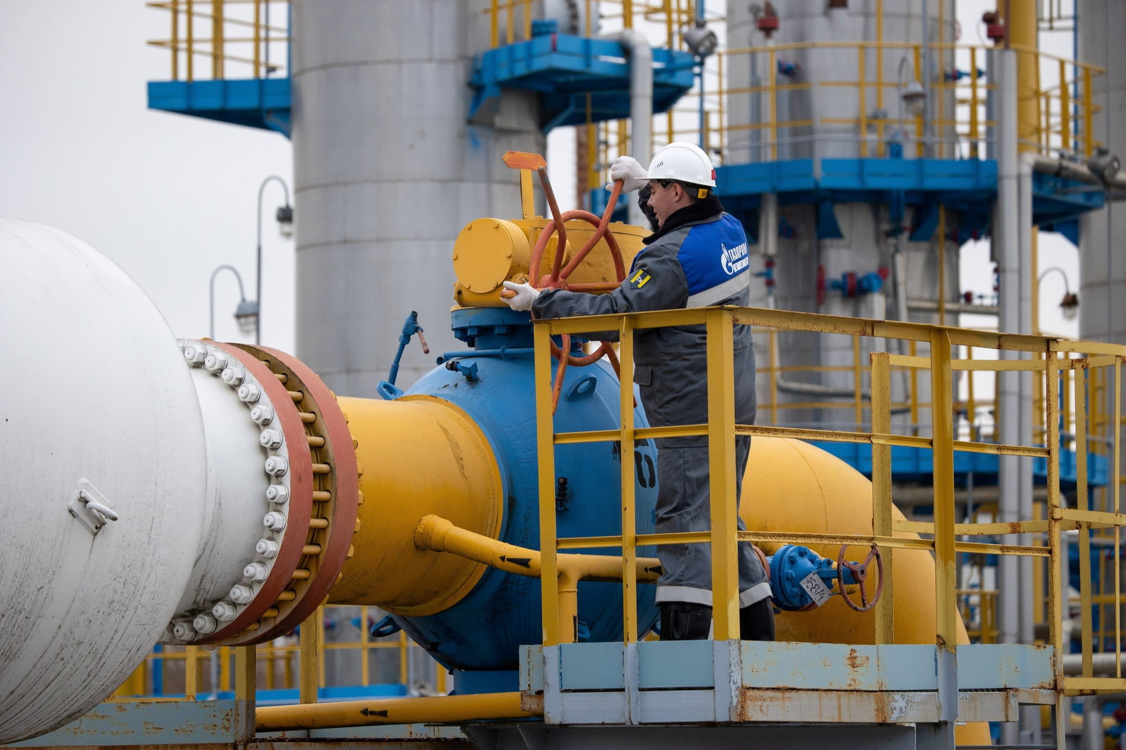 A worker turns a wheel connected to a large gas pipe at a Gazprom storage facility