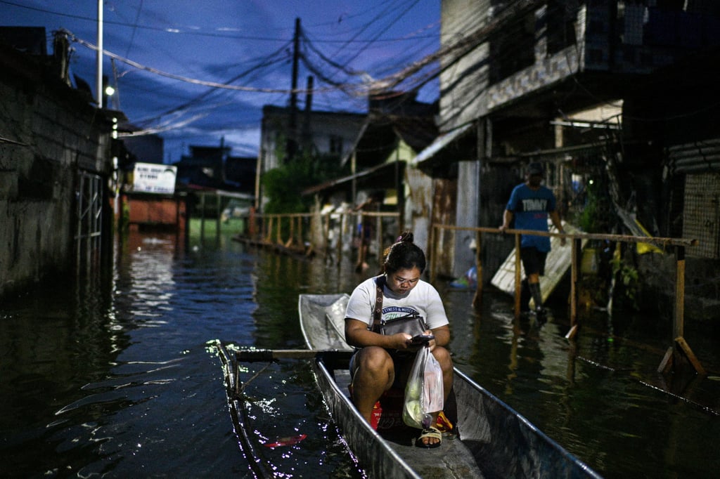 A woman uses her mobile phone as she rides on a boat to cross a flooded street following then-Severe Tropical Storm Bualoi in Binan, Laguna province in the Philippines on Friday. Photo: Reuters
