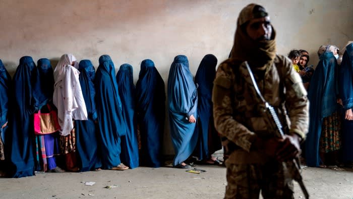 A Taliban fighter stands guard as women wait to receive food aid in Kabul