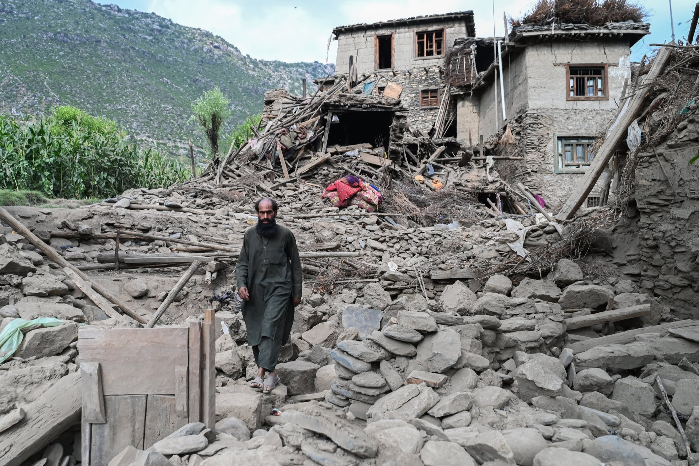 A man walks across rubble in front of a house partially destroyed by the earthquake