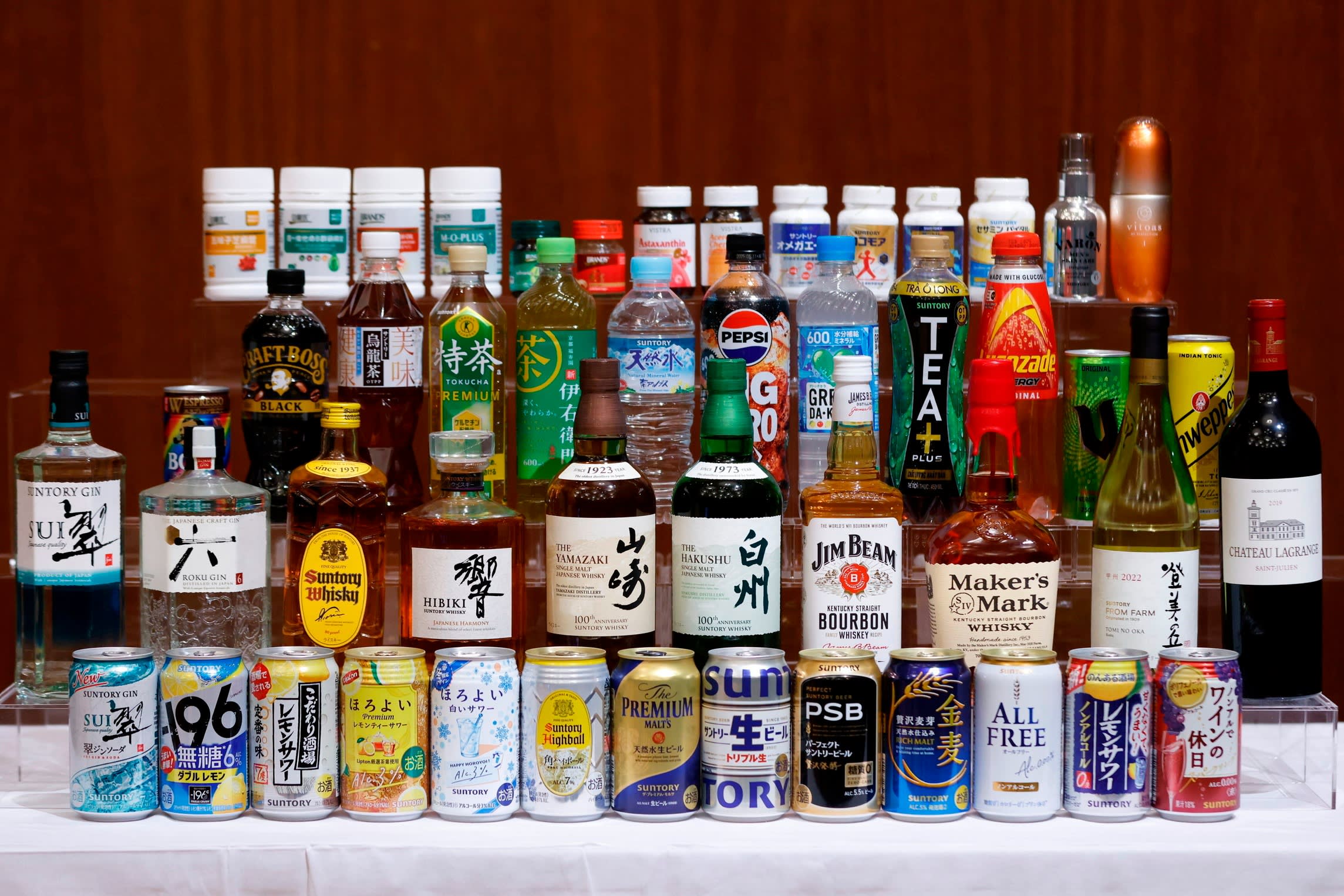 Bottles and cans of Suntory beverages, including whisky, gin, tea, water, and soft drinks, arranged on a table for display.