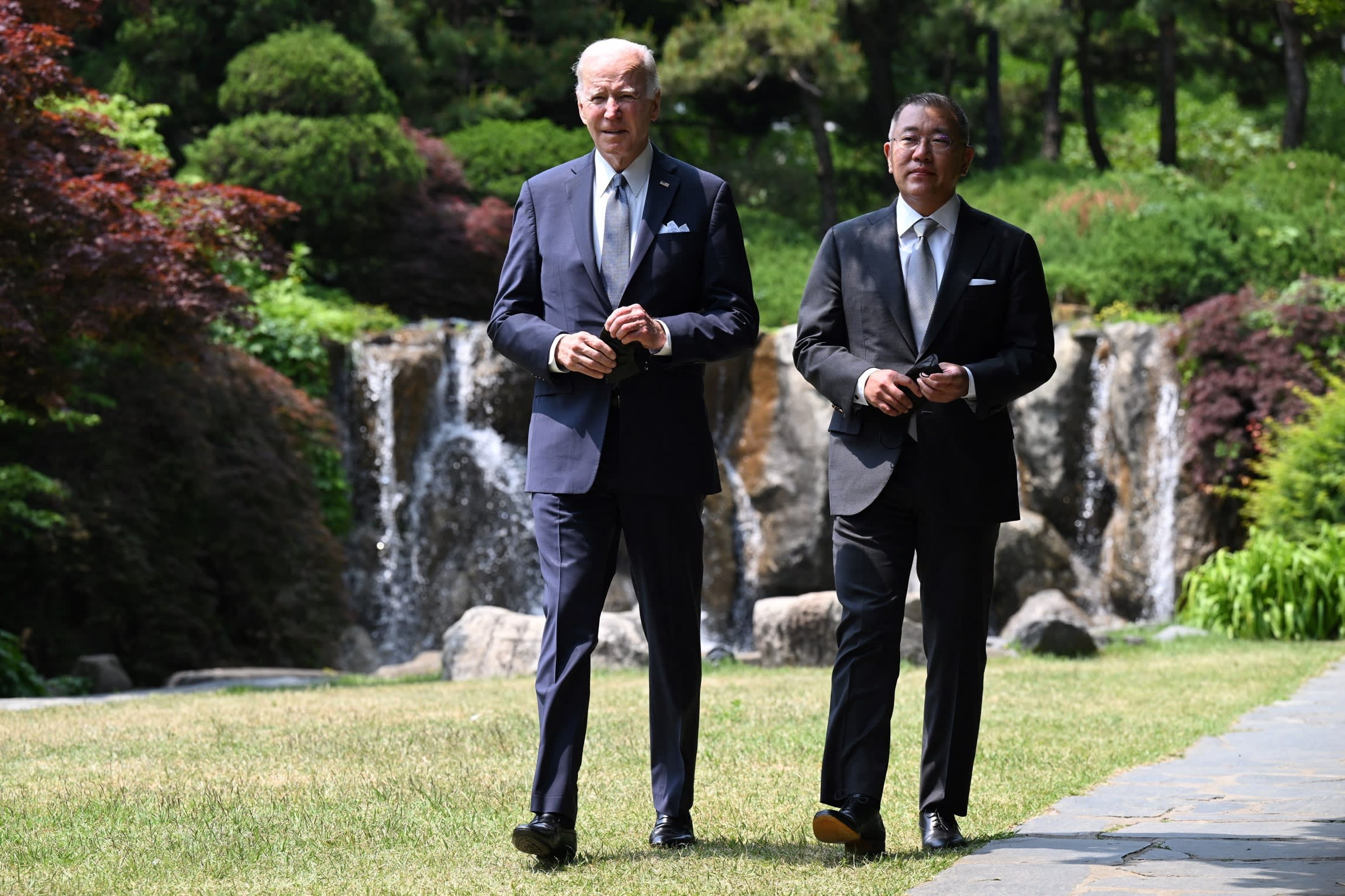 Joe Biden and Chung Eui-sun walk together in a garden with a waterfall in the background.