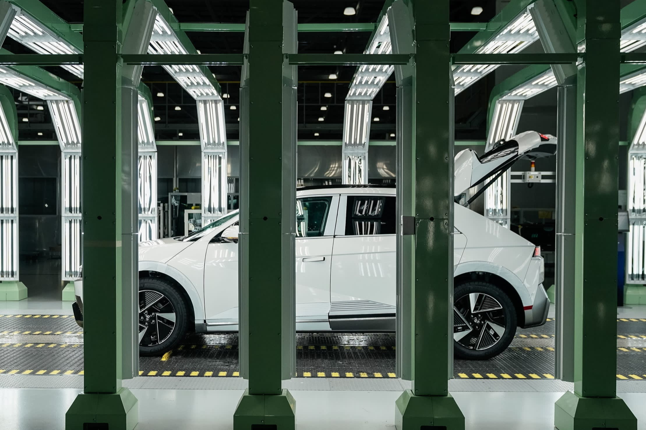 A white Hyundai electric vehicle with its rear hatch open sits in a brightly lit inspection tunnel at the Metaplant facility in Georgia