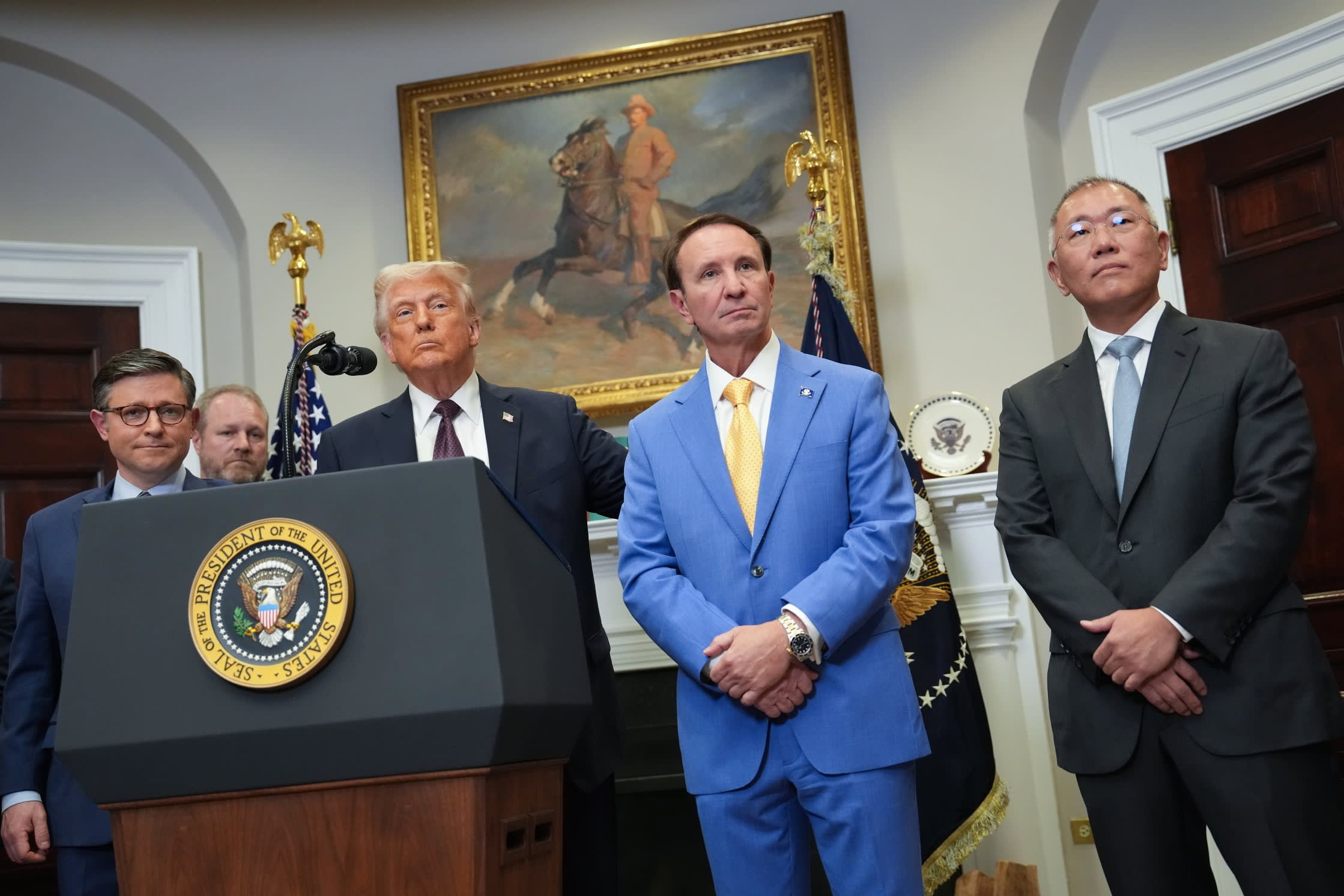Donald Trump stands at a podium flanked by Speaker of the House Mike Johnson, Louisiana governor Jeff Landry,and Hyundai chair Chung Eui-sun at a White House event. Ascension Parish President Clint Cointment is at the back