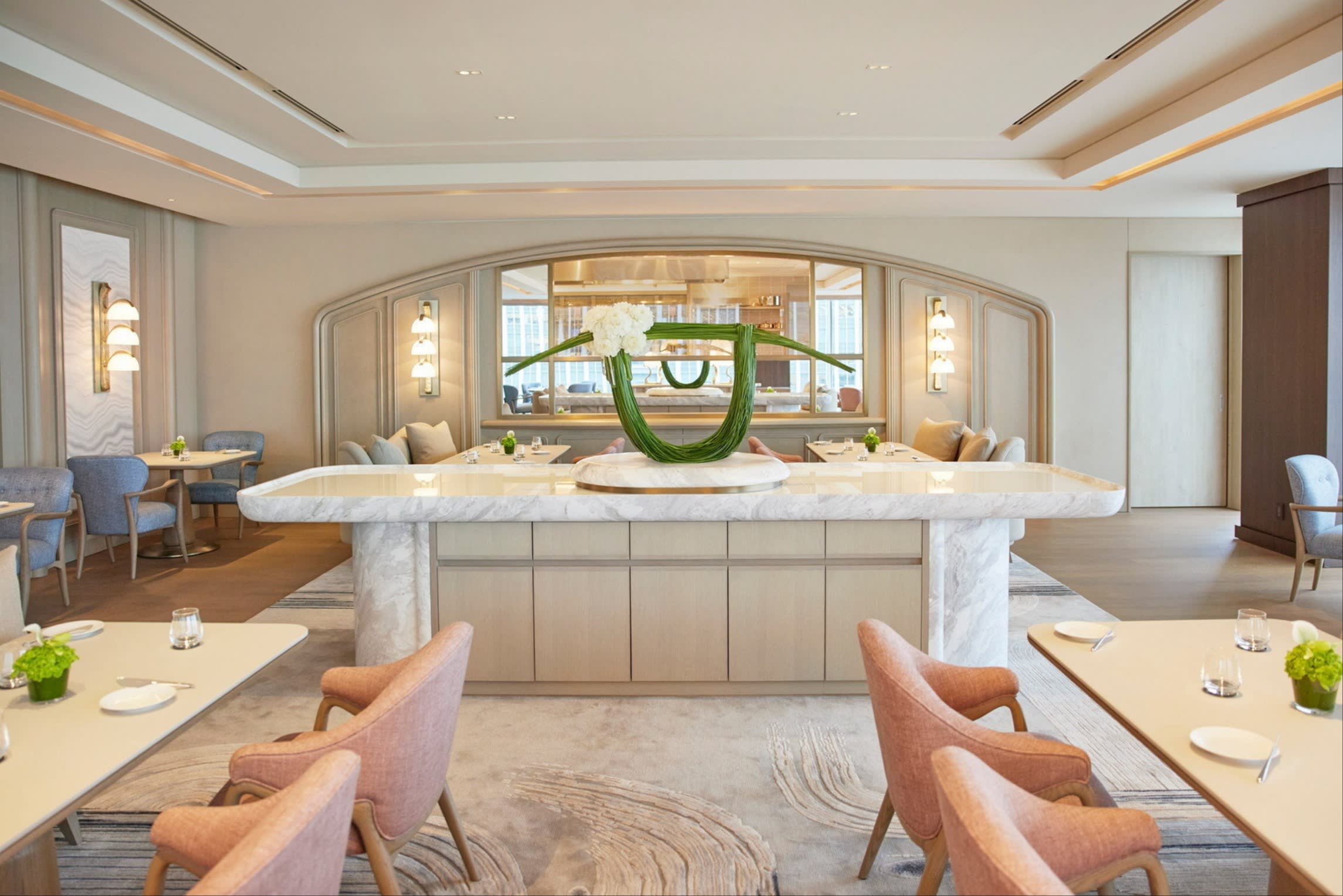 The spacious, elegantly decorated interior of Sézanne, with pastel-coloured chairs, white marble accents, and a large modern floral arrangement as thcentrepiecece.