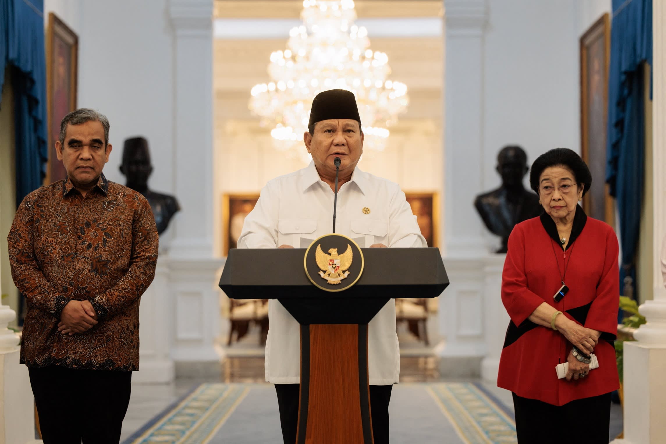 Prabowo Subianto speaks at a podium flanked by two political party leaders during a press conference at the Presidential Palace.