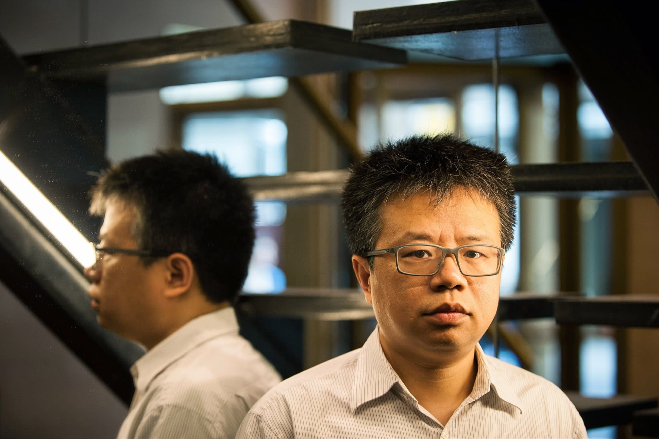Li Qiang stands indoors near a staircase, with his reflection visible in a mirror behind him.