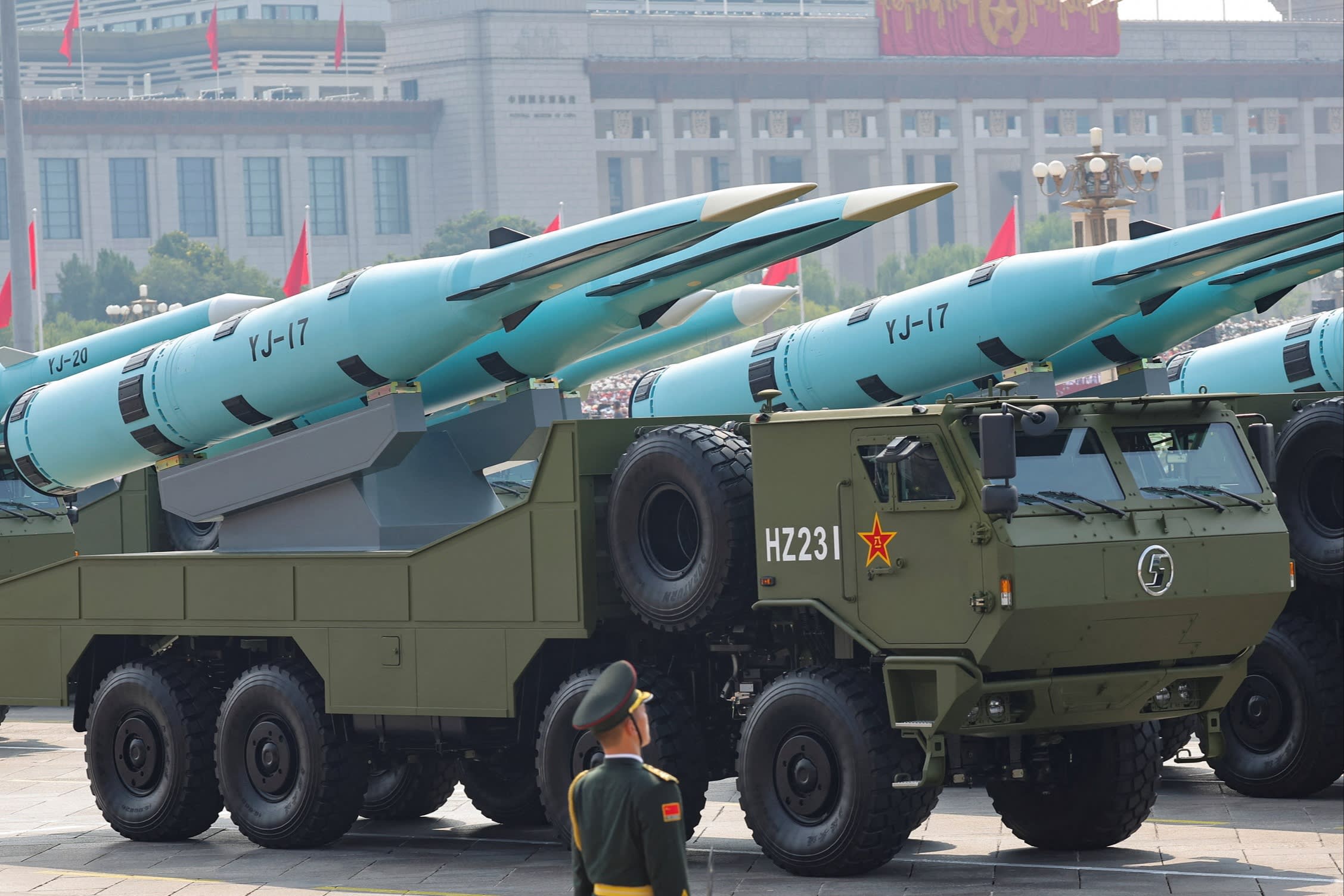 A member of the People's Liberation Army stands in front of military vehicles carrying YJ-17 hypersonic anti-ship missiles during a parade.
